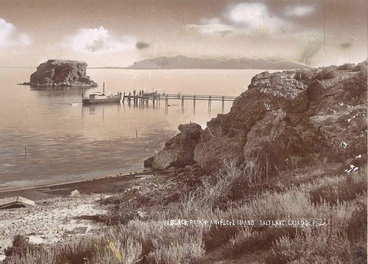 Historic photograph by C.R. Savage of Black Rock and Antelope Island on Great Salt Lake, with a steamboat at a wooden pier